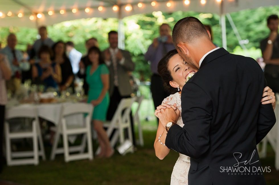 Couple dancing at a wedding reception under string lights, with guests seated in the background