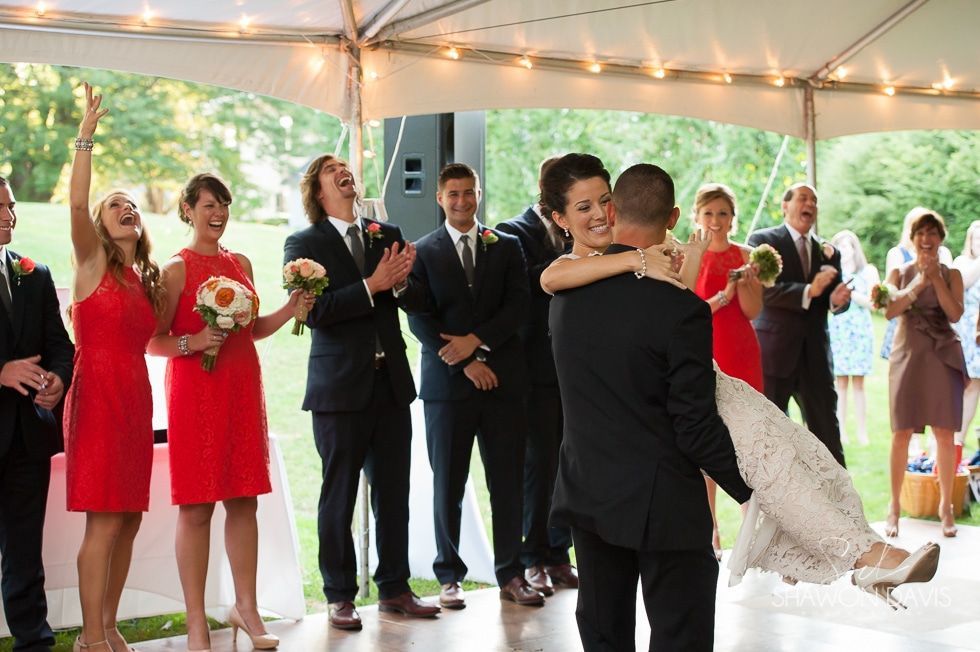 Wedding couple embracing under a tent while guests applaud nearby