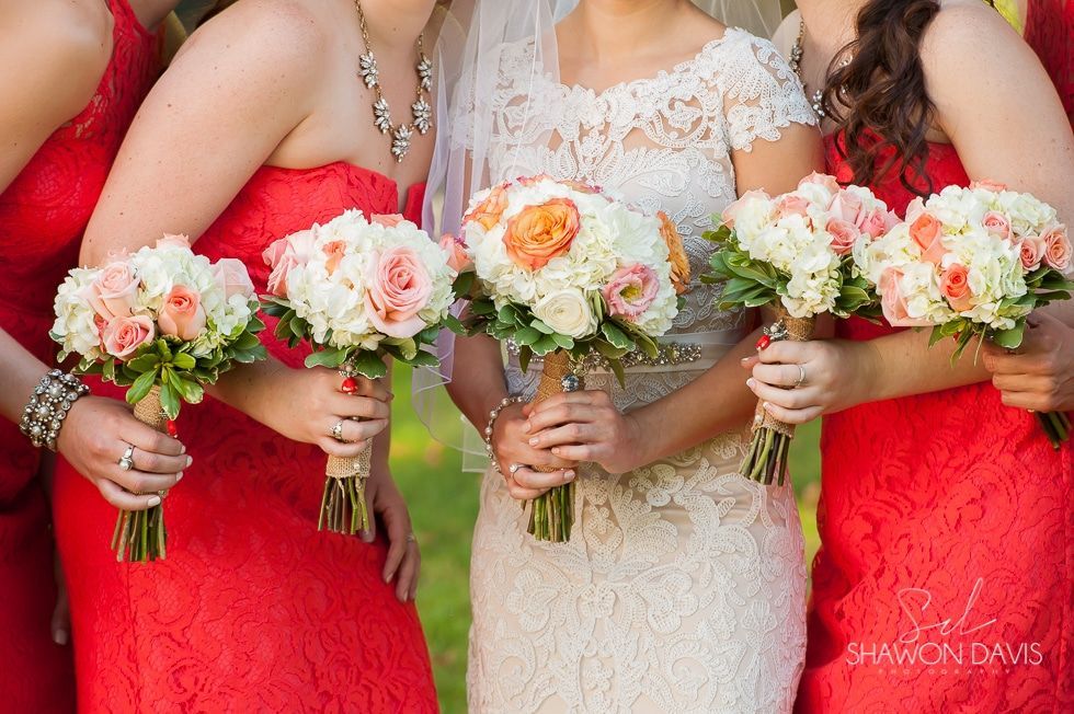 Three women in red and ivory dresses holding matching white and pink flower bouquets