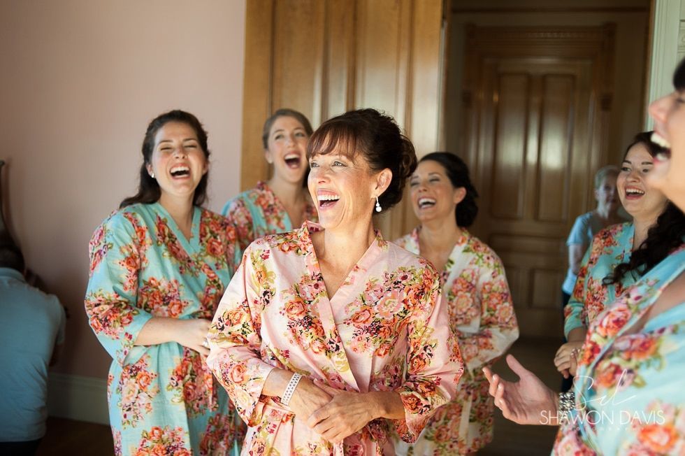 Women in floral robes laughing together in a doorway at a wedding prep event