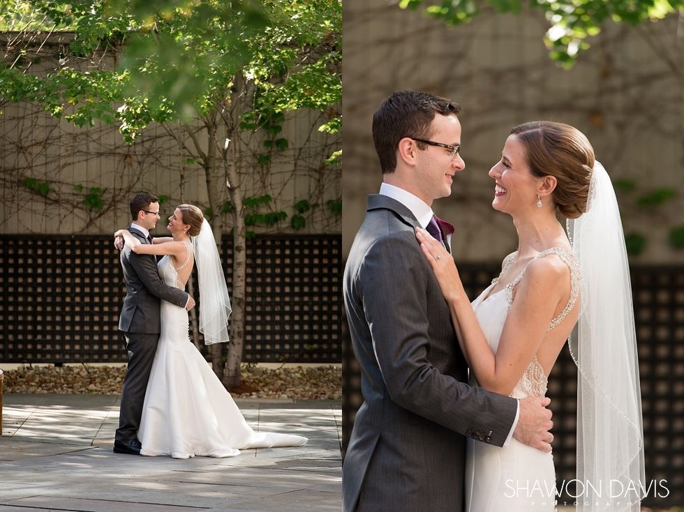Two wedding couples embracing outdoors in formal attire under green trees.