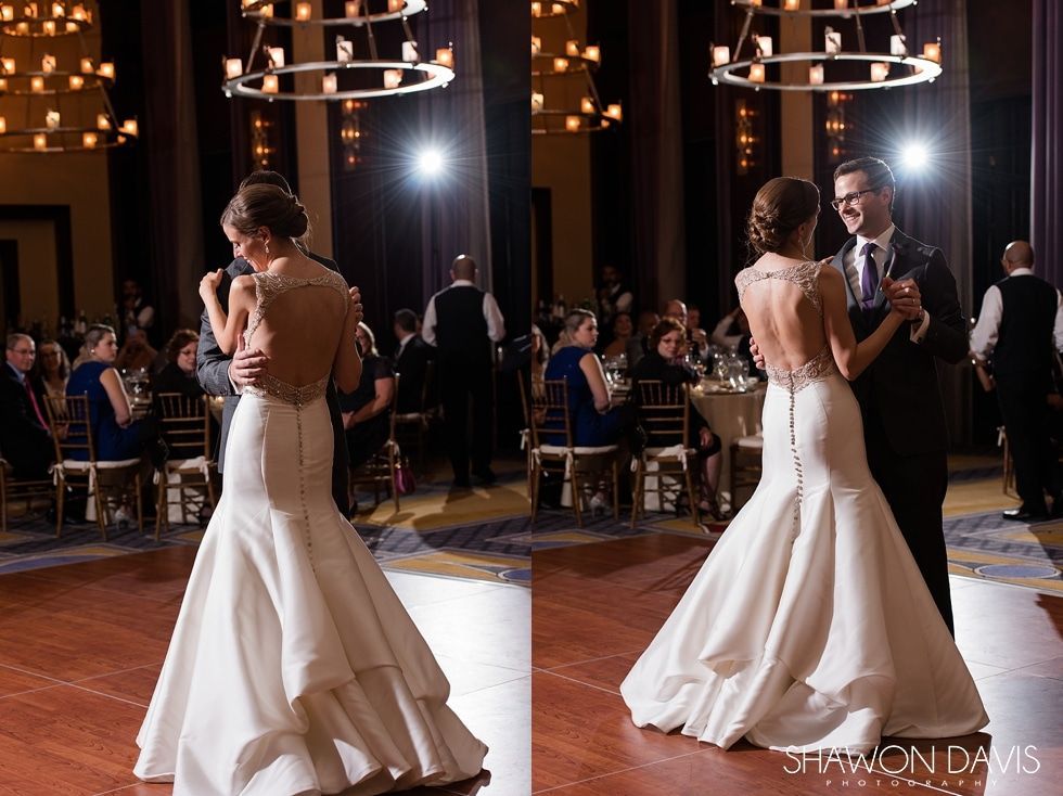 Bride in a white gown dancing with a groom in a dark suit at a warmly lit reception