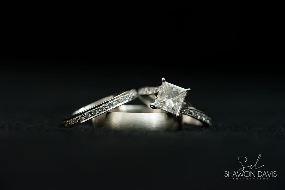 Silver engagement ring with a square-cut diamond and pavé band on a dark background