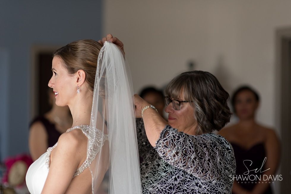 Bride with veil being adjusted by a woman indoors at a wedding preparation event