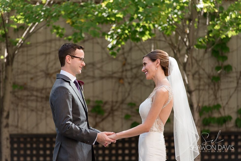 Bride and groom holding hands and smiling outdoors beneath green trees