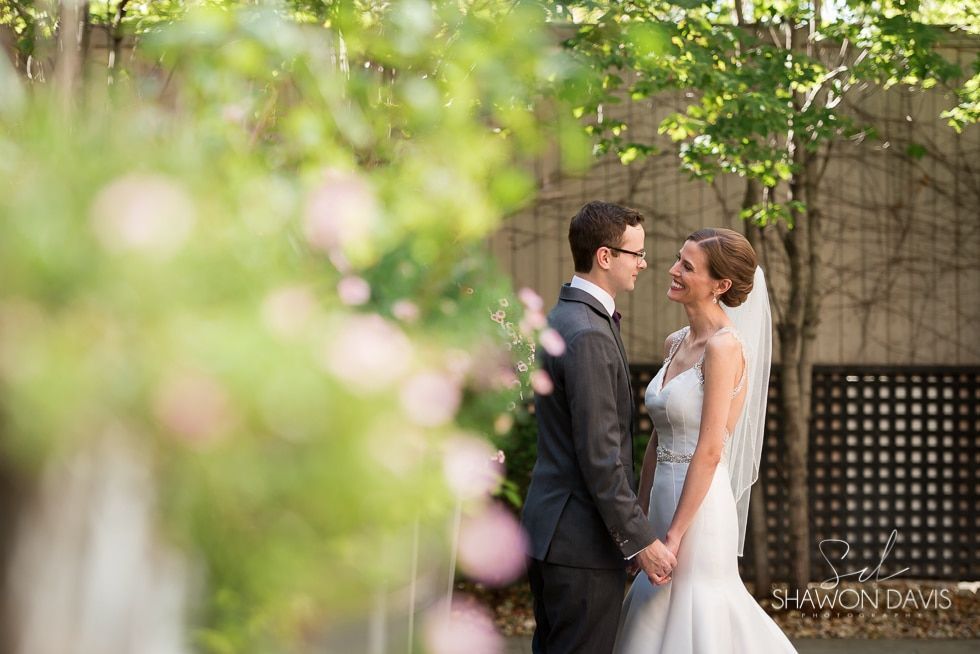 Bride and groom holding hands and smiling in a garden with soft pink blossoms