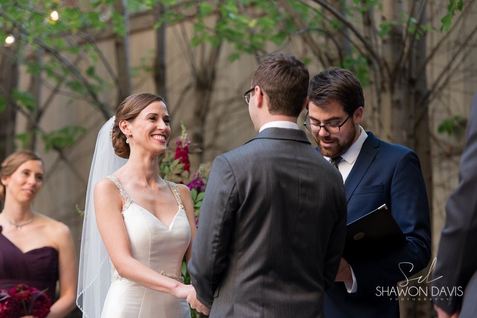 Bride smiling at groom during outdoor wedding ceremony with officiant nearby