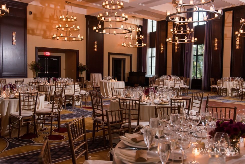 Elegant banquet hall with round tables, gold chairs, chandeliers, and set place settings