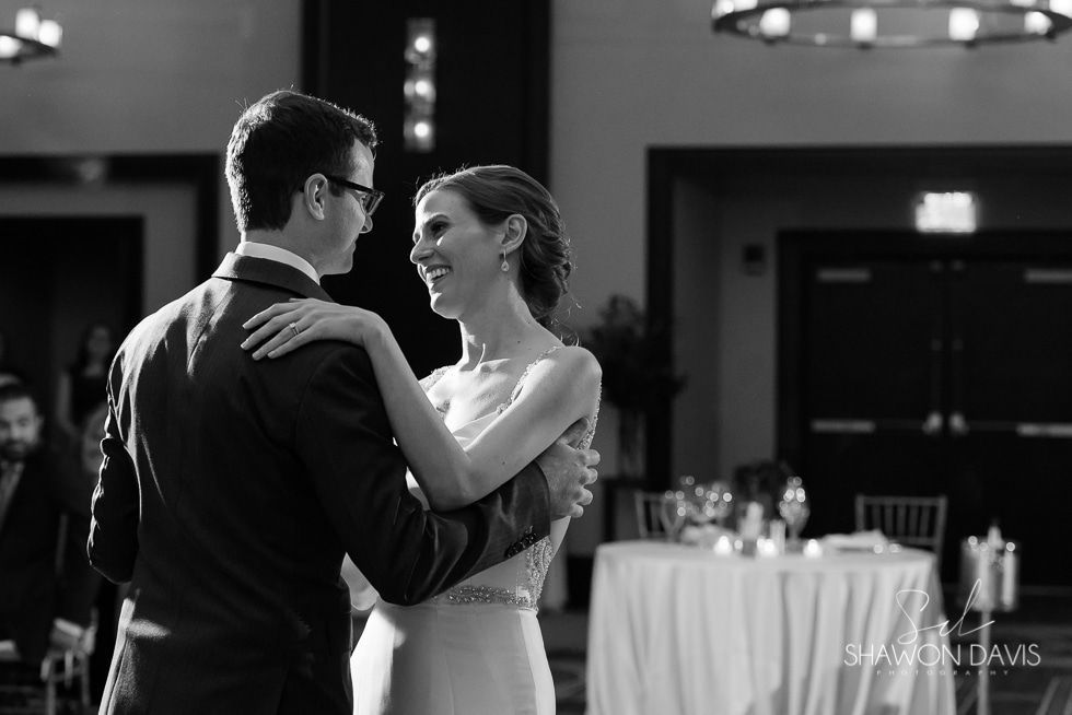 Couple dancing at a formal reception, smiling and facing each other in black-and-white.