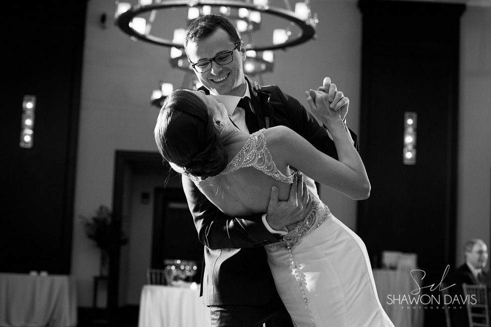 Couple dancing at a wedding, smiling and embracing under a chandelier.