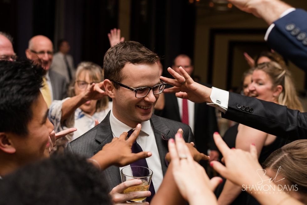 Crowd reaching toward a smiling man in glasses at an indoor gathering