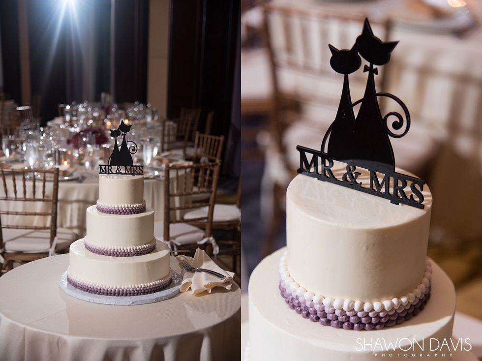 Two white tiered wedding cakes with black cat toppers on decorated dessert tables