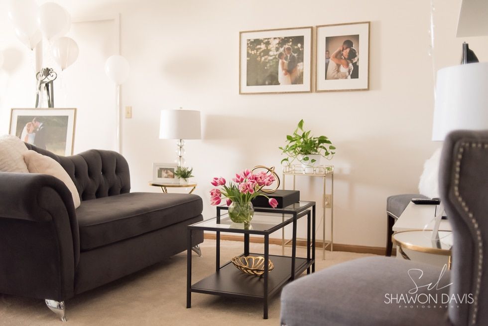 Cozy living room with dark sofa, glass coffee table, flowers, lamps, and framed wall art