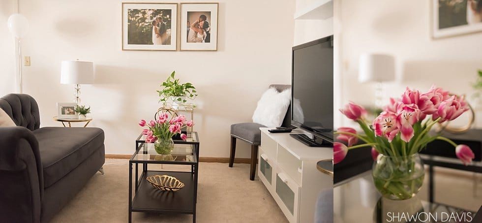Bright living room with gray sofa, white TV stand, coffee table, and pink flowers by the window.