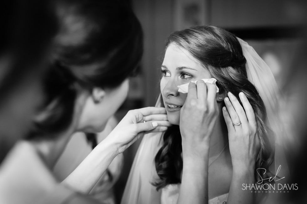 Bride having makeup applied while looking into a mirror, black-and-white close-up