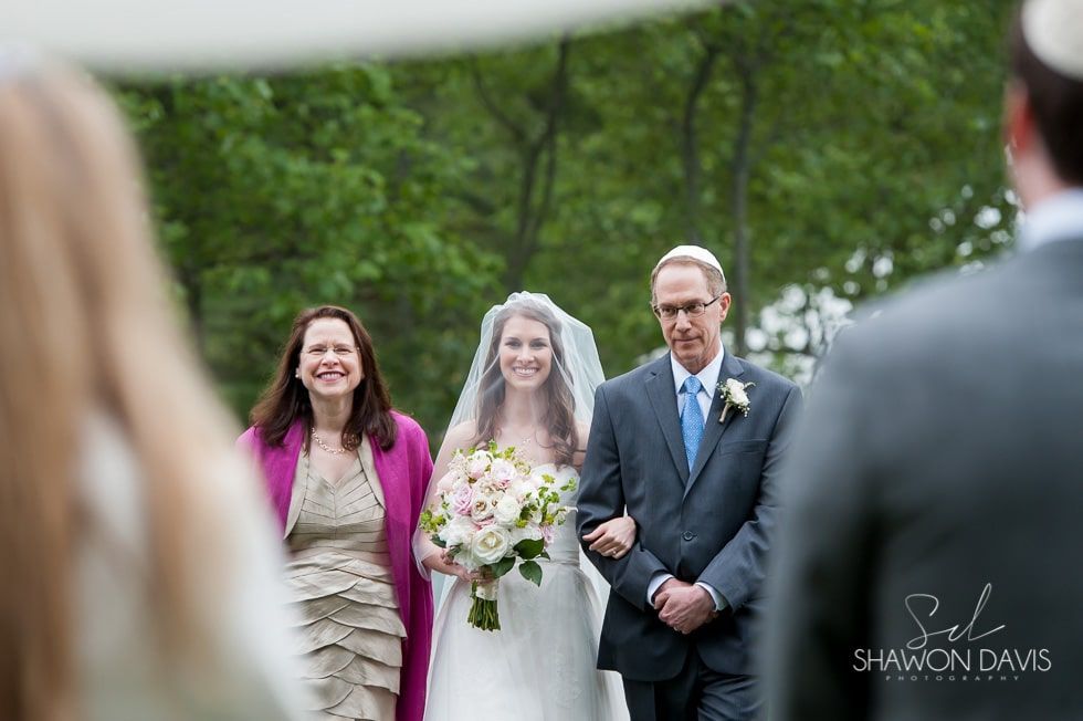 Bride and groom with bridesmaid, standing outdoors at a wedding ceremony