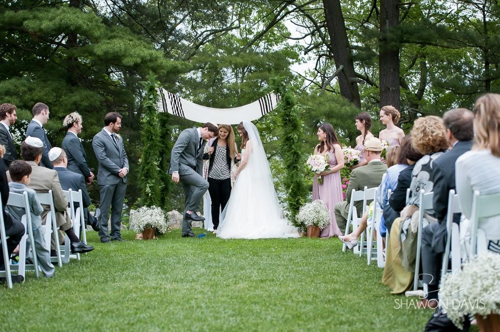 Outdoor wedding ceremony on a green lawn, bride and groom under a white arch, guests seated on both sides.