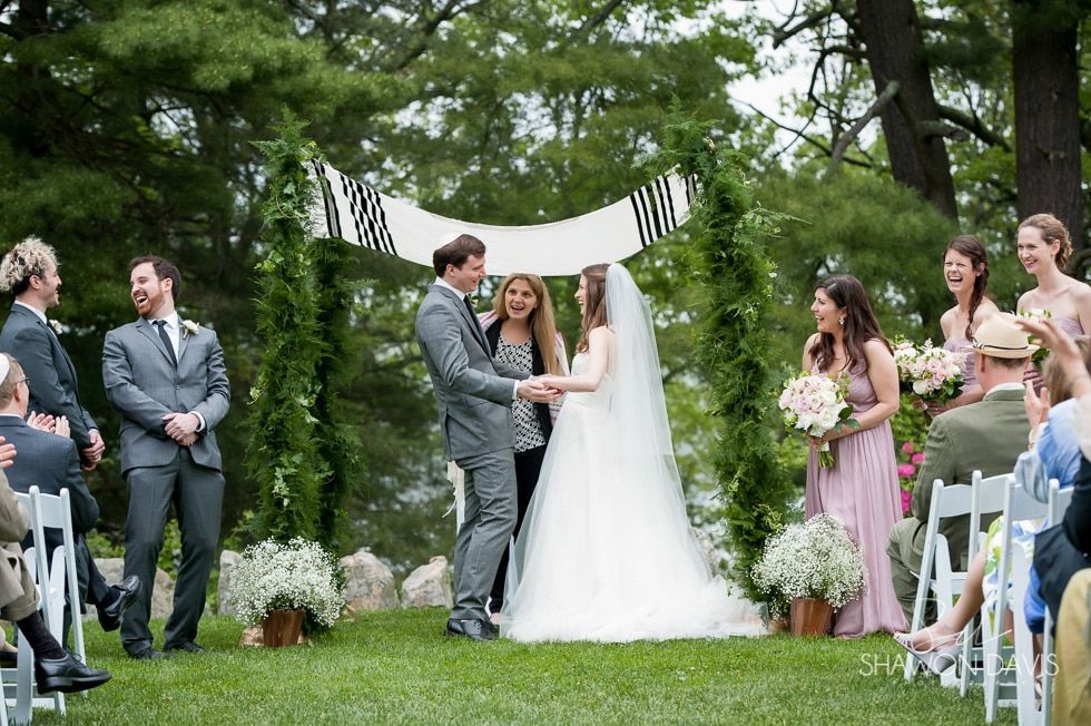 Bride and groom exchanging vows under a striped canopy in a garden wedding ceremony.