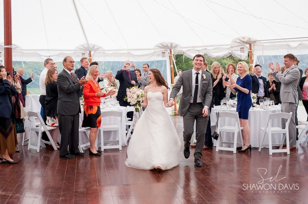 Bride and groom walking down the aisle at a tented wedding reception, guests applauding