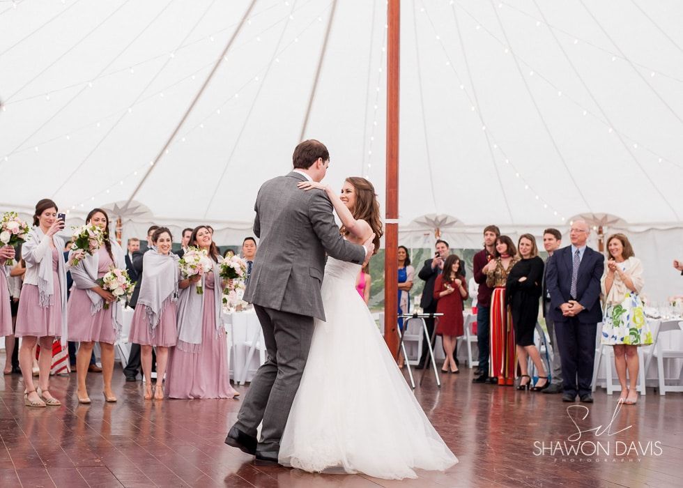 Wedding couple dancing under a white tent, with guests gathered around them