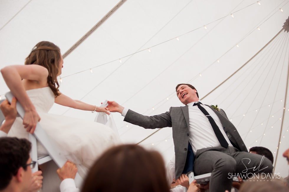 Bride and groom smiling and holding hands during a wedding celebration inside a tent