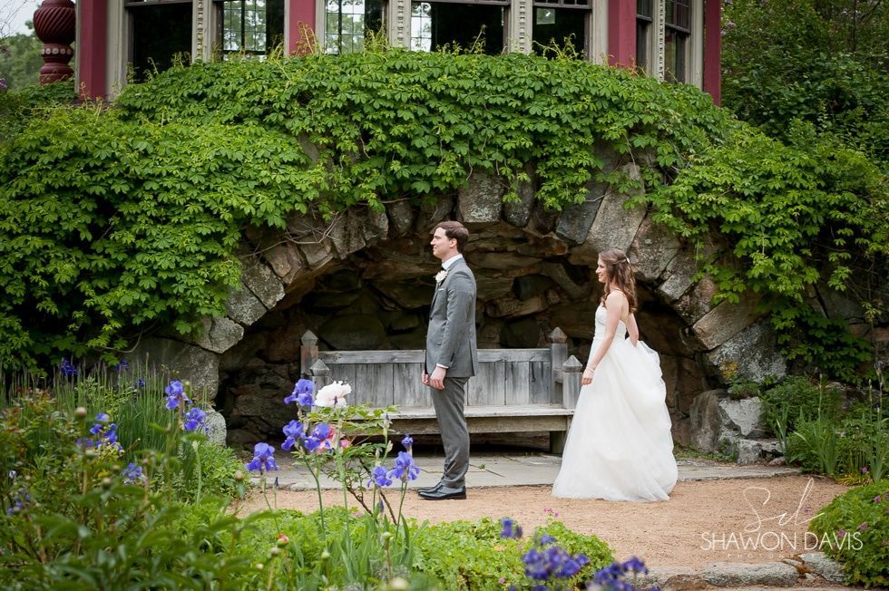 Bride and groom standing in a garden before a stone arch covered in greenery