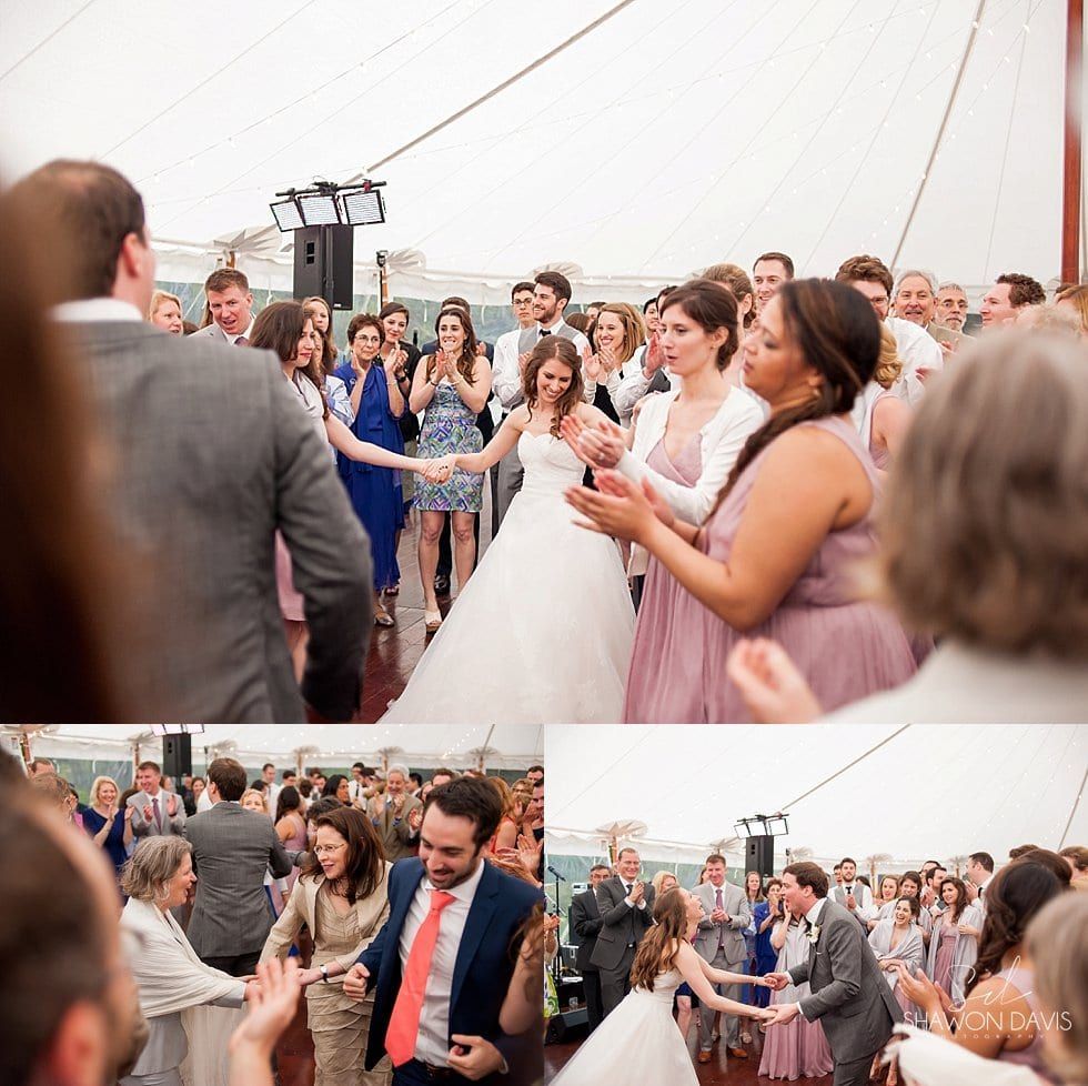 Wedding guests applauding under a tent as the bride and groom walk through the crowd.