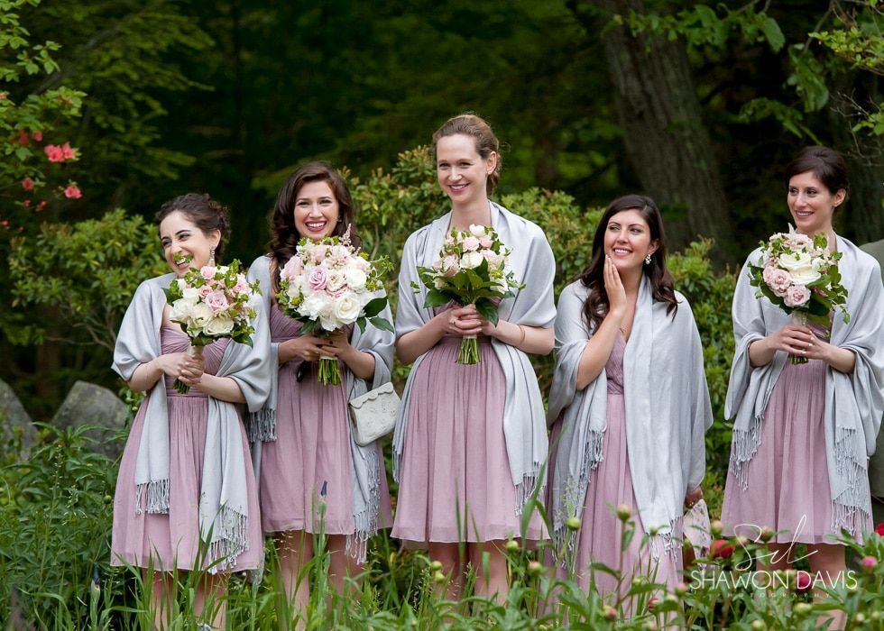 Five women in lavender dresses and shawls holding white flower bouquets in a garden