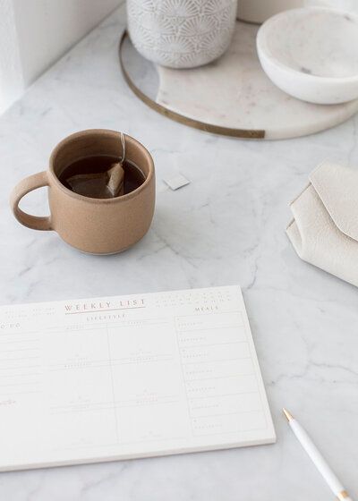 Minimal desk with a brown mug, open notebook, pencil, and white decor on a marble surface