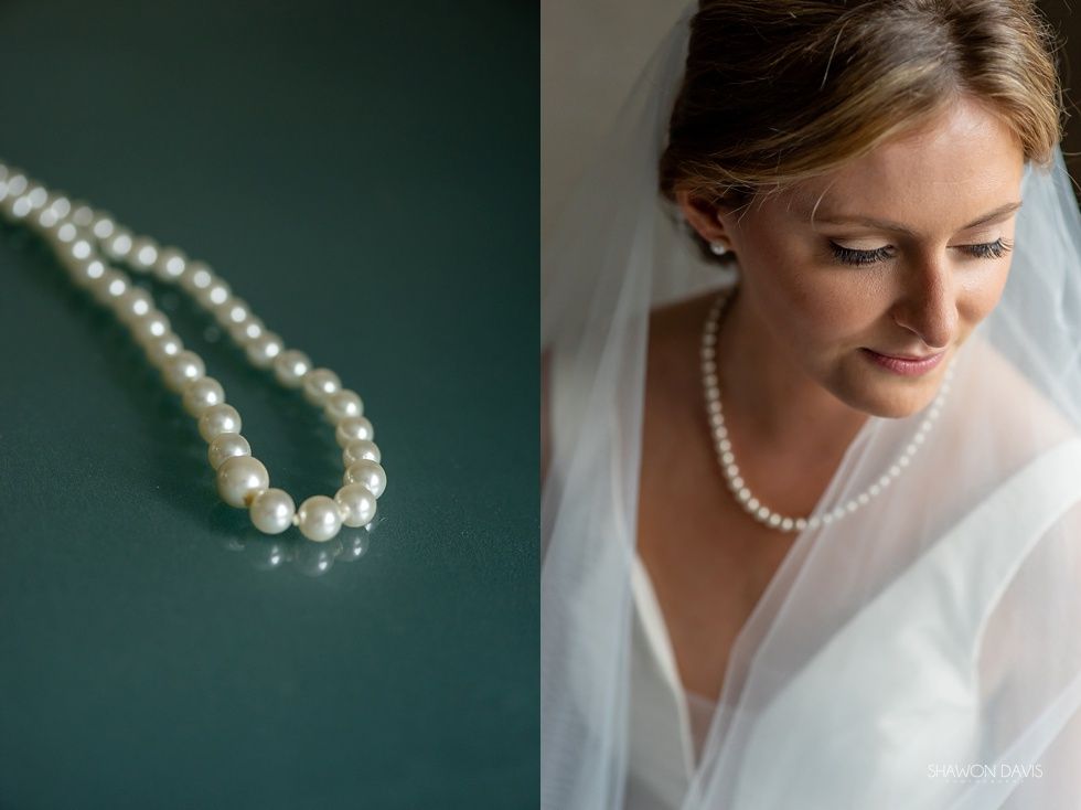 Pearl necklace beside a bride in a white veil, looking down softly.