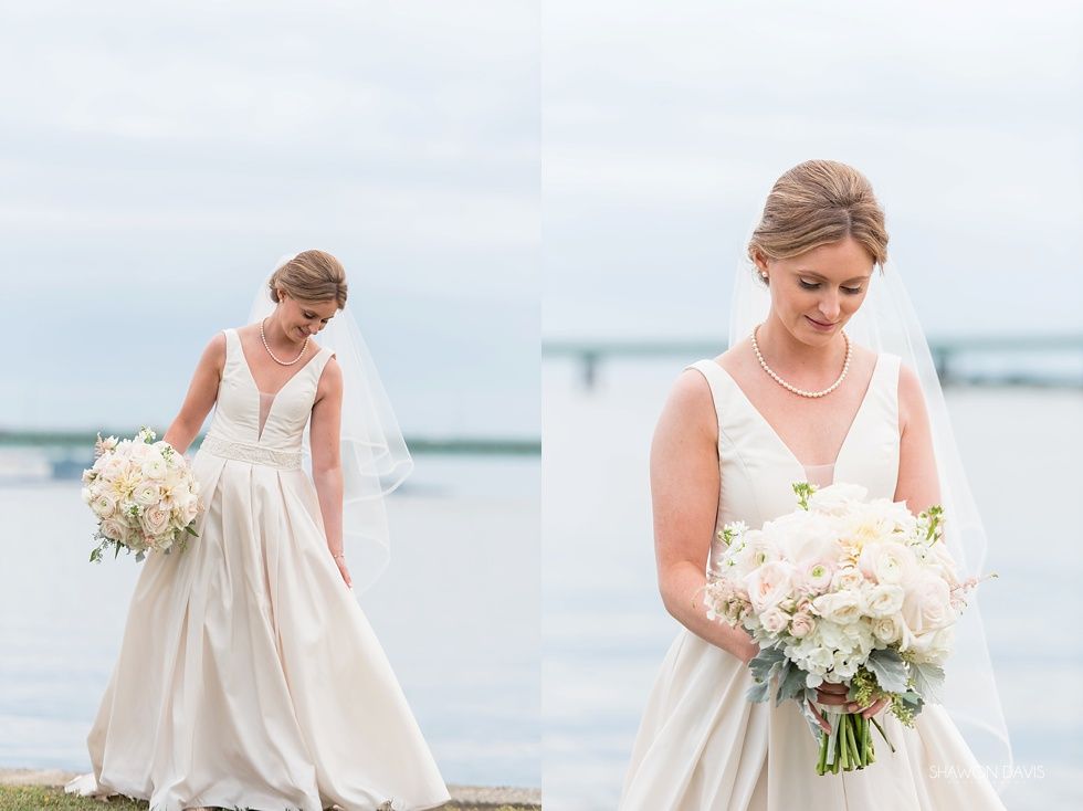 Two brides in white dresses holding bouquets by the water, one looking down, one standing in the background