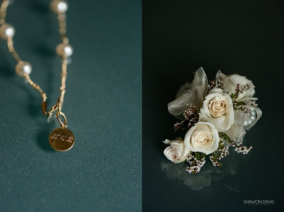 Gold pendant necklace beside a white rose floral corsage on a dark background