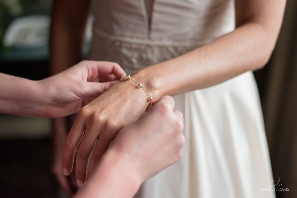 Hands fastening a delicate gold bracelet on a person in a white dress.