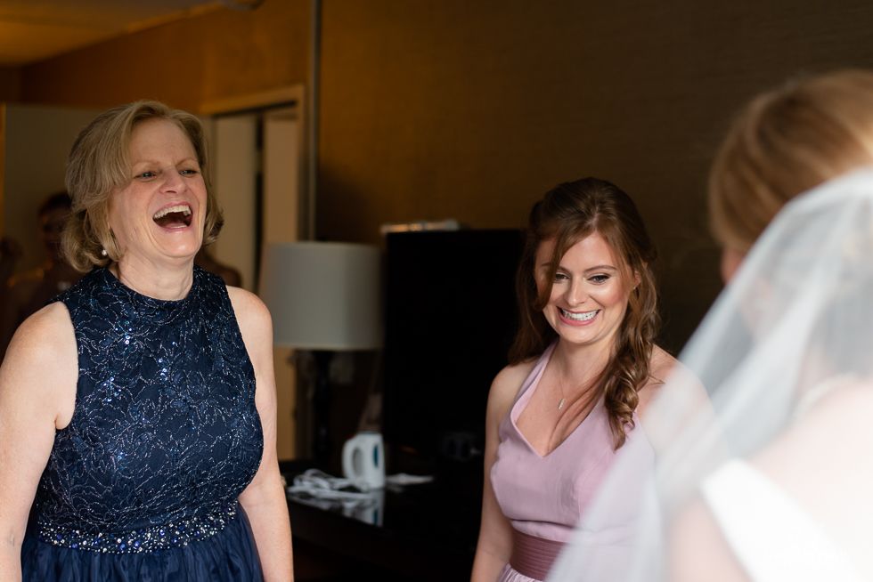 Two smiling women at a wedding, with the bride in a veil in the foreground