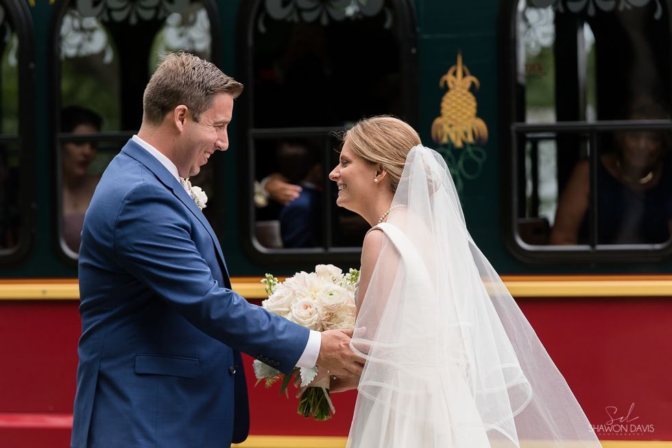 Bride and groom exchanging hands beside a train, with the bride holding a bouquet and wearing a veil