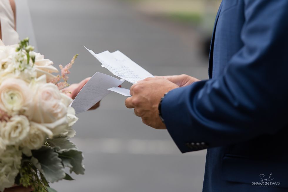 Hands in a blue suit holding a folded paper near a bouquet of white flowers outdoors