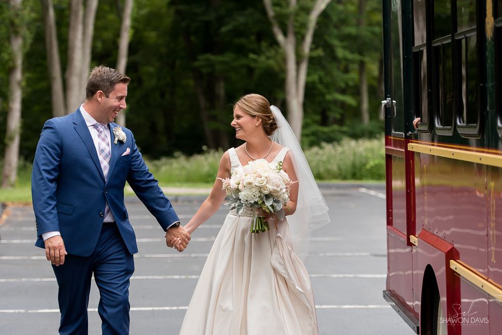 Bride and groom holding hands outdoors beside a red tram, walking together in a park-like setting