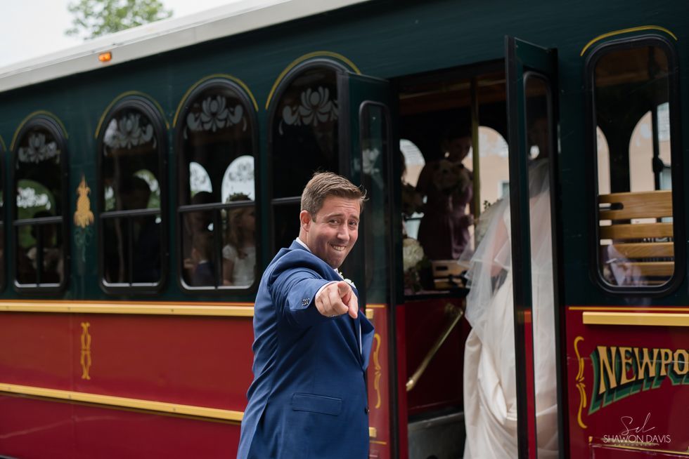 Man in blue suit pointing from the doorway of a red and green vintage train carriage