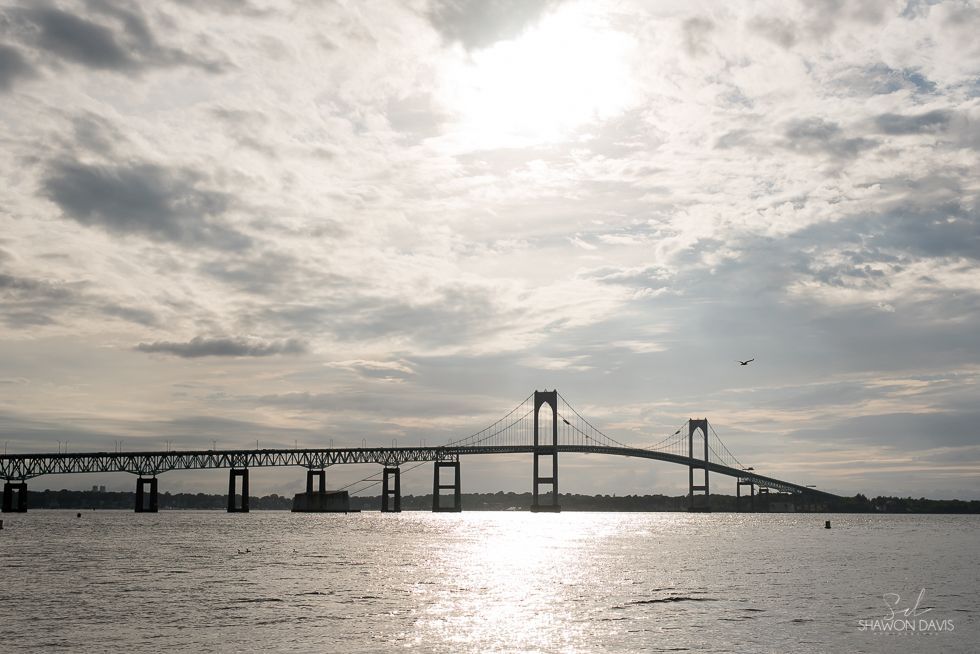 Suspension bridge over water under a cloudy sky with sunlight reflecting on the surface