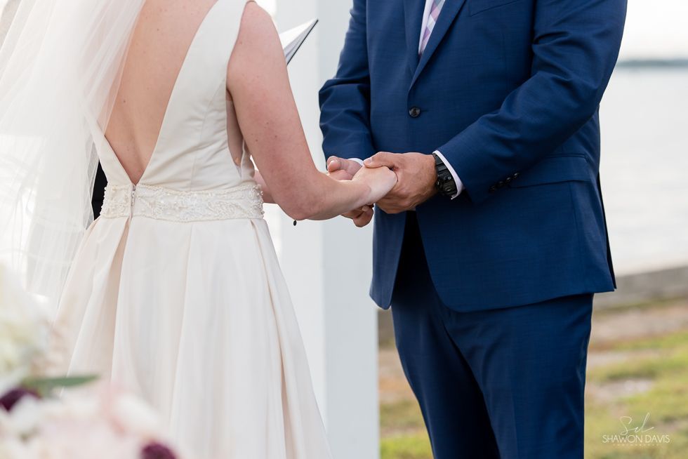 Bride in white gown and groom in blue suit holding hands outdoors