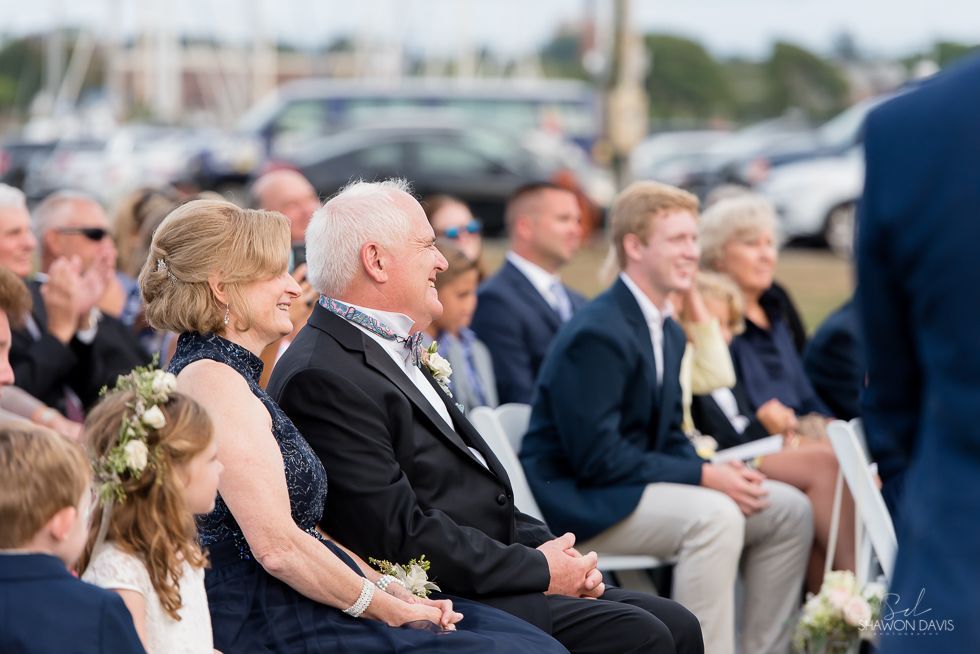 Seated guests at an outdoor event, dressed formally and watching the ceremony.