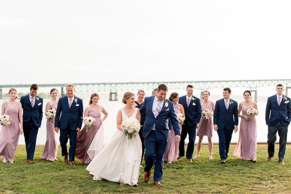 Wedding party walking on grass outdoors, with bride in white dress and groom in blue suit at center