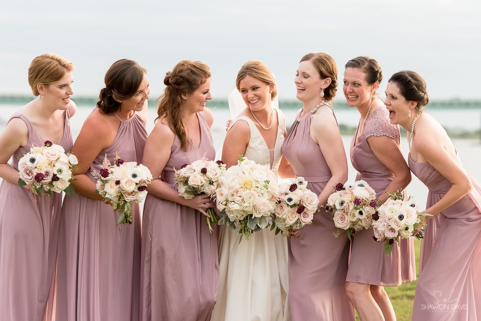 Bridesmaids in blush dresses holding bouquets around a bride in white outdoors at sunset