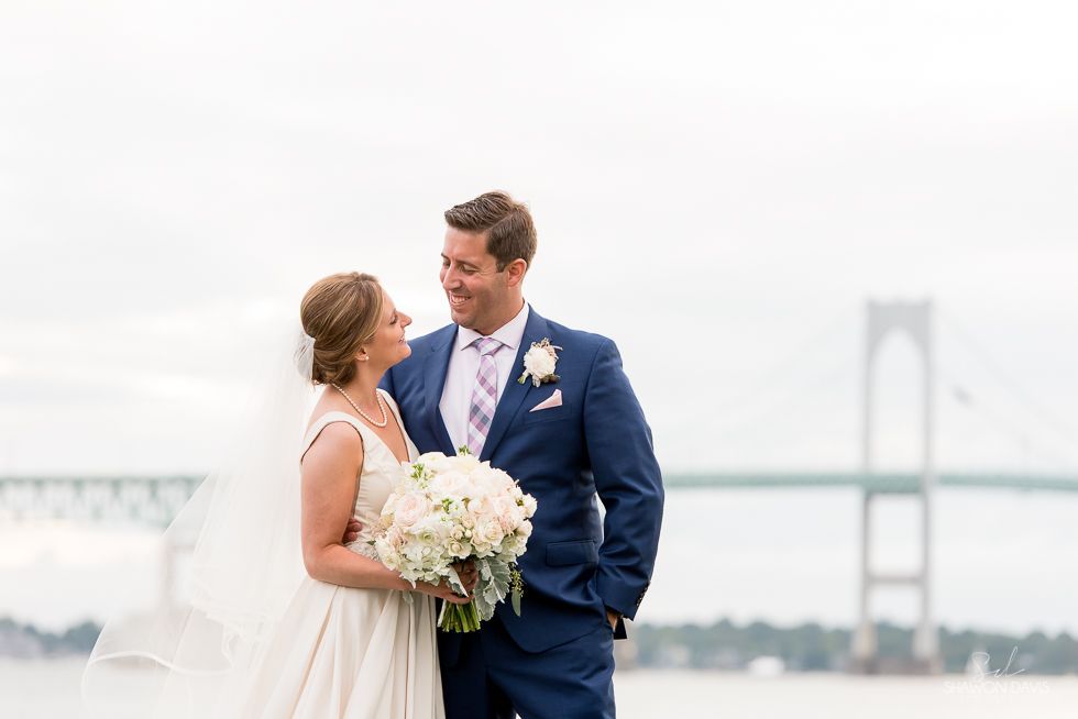 Bride and groom sharing a moment by a bridge, with a bouquet and foggy waterfront backdrop