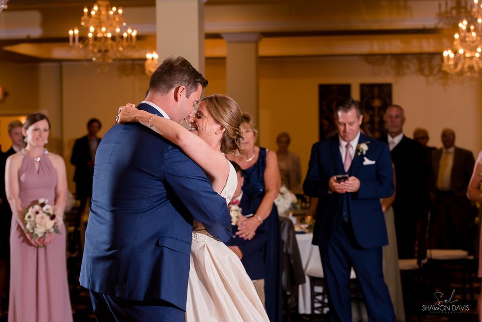 Couple slow-dancing at a wedding reception while guests watch in a warmly lit ballroom