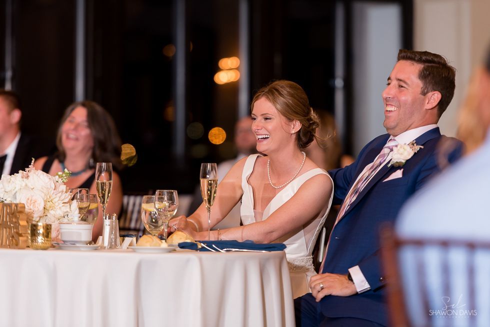 Guests smiling at a formal banquet table, with a man in a blue suit and woman in a white dress in the foreground