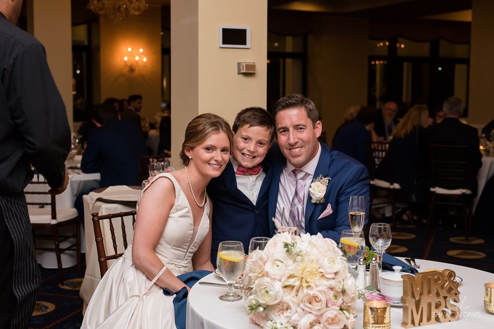 Three smiling guests at a wedding reception table with flowers and drinks