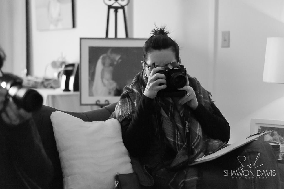 Person holding a camera while seated on a couch in a living room, black-and-white scene