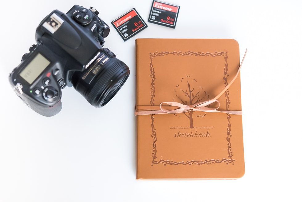 Camera beside a brown gift-wrapped notebook tied with twine on a white background