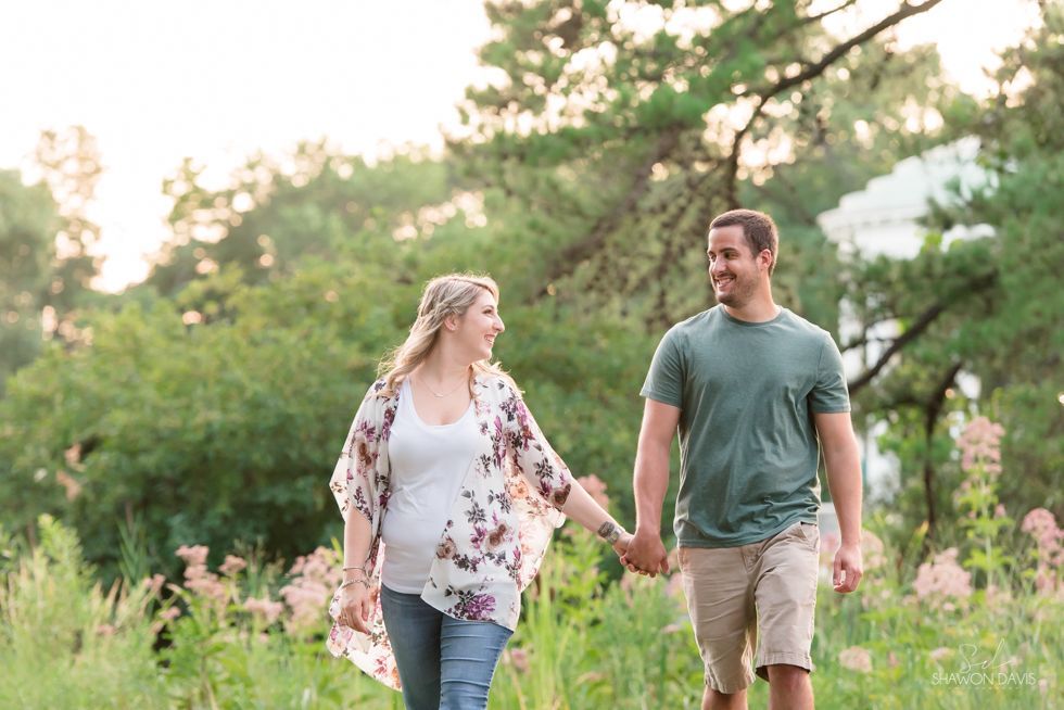 Couple holding hands and walking through a lush green field at sunset